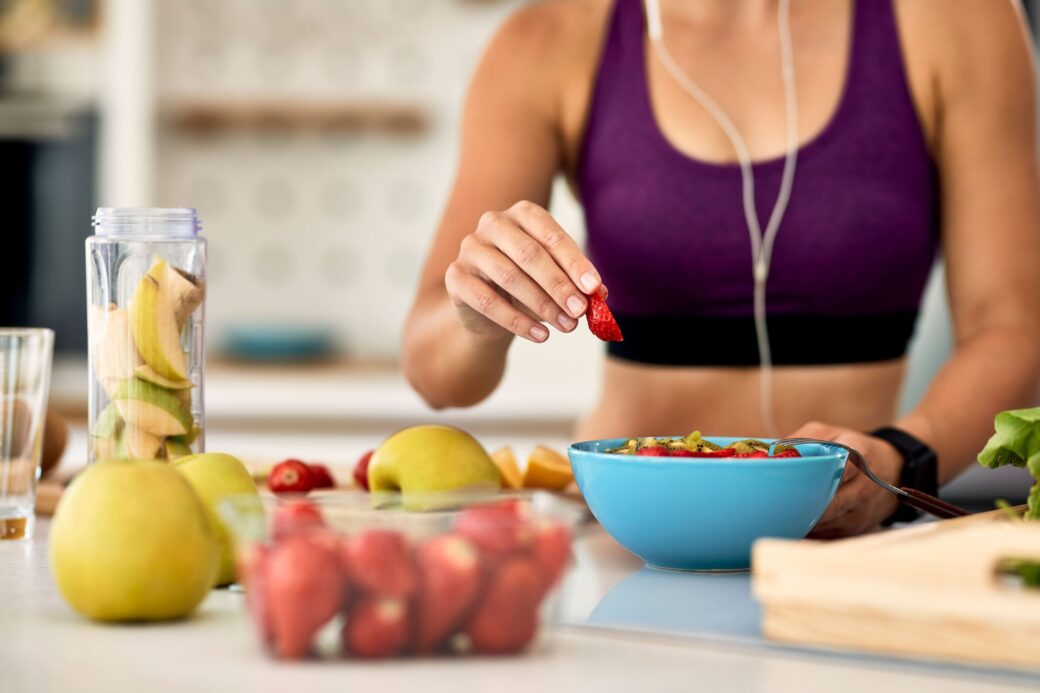nutricion deportiva,primer plano de una mujer atlética añadiendo fresas mientras prepara una ensalada de frutas en la cocina